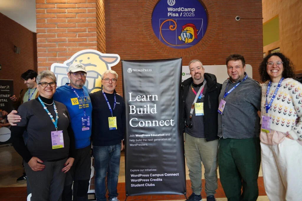 Group of people smiling at WordCamp Pisa 2025 event with a WordPress banner.